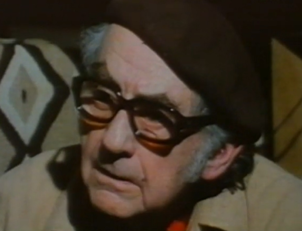 Screenshot: Man Ray wearing grey coat and hat is looking at side - from Man Ray- Prophet of the Avant-Garde (1997)