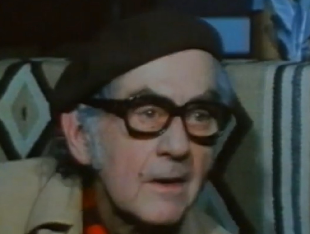 Screenshot: Man Ray wearing grey coat and hat is looking at side - from Man Ray- Prophet of the Avant-Garde (1997)