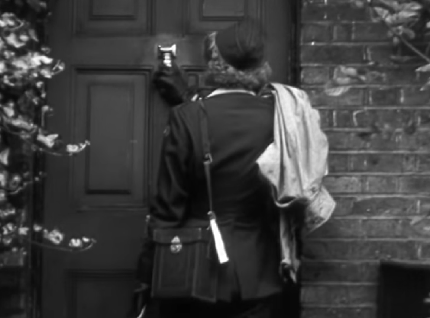 Screenshot: B&W Lee Miller wearing white shirt and black jacket is standing in front door - from Lee Miller: Through the Mirror (1955)