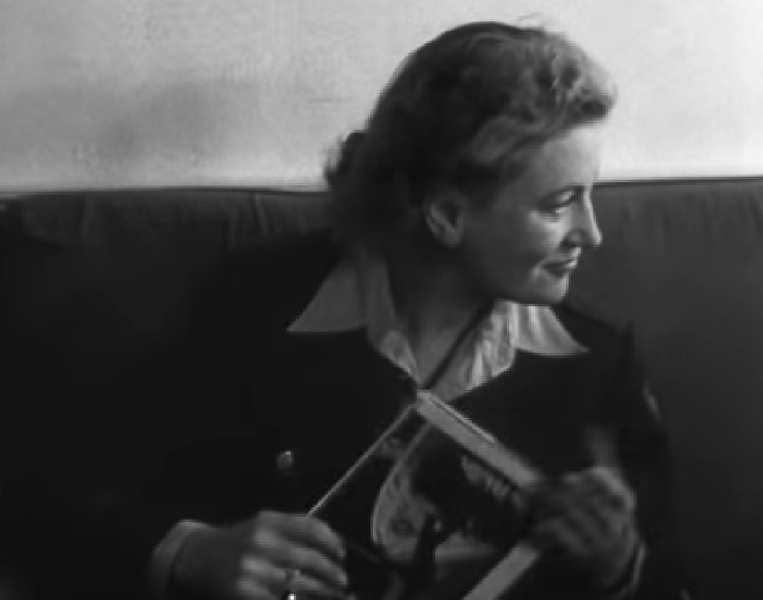 Screenshot: B&W Lee Miller seating inside and holding a magazine - from Lee Miller: Through the Mirror (1955)
