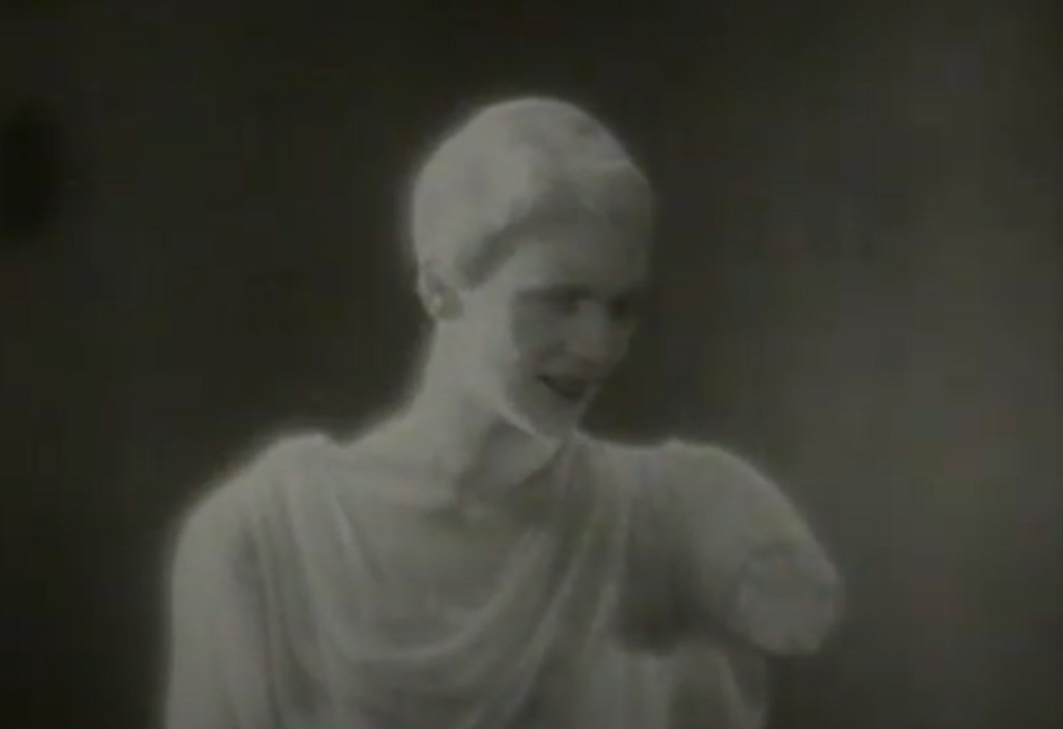 Screenshot: B&W Lee Miller wearing white make up at her is smiling and looking at from - Lee Miller: Through the Mirror (1955)