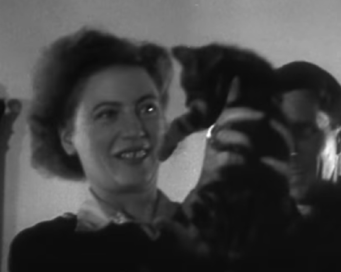 Screenshot: B&W Lee Miller is holding a small cat and smiling standing next to Roland Penrose - from Lee Miller- Through The Mirror (1955)
