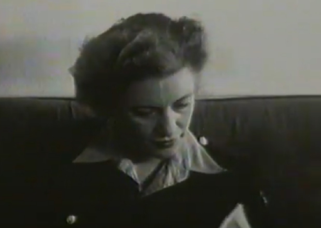 Screenshot: B&W Lee Miller wearing white shirt and black sweater is looking down - from Lee Miller: Through the Mirror (1955)