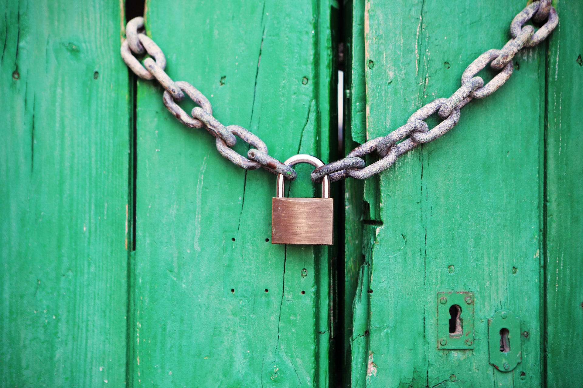 brass colored metal padlock with chain placed on a green door