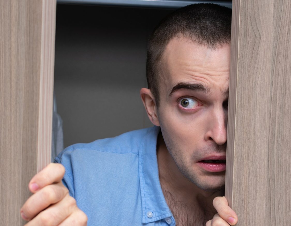 Young man wearing blue shirt is hiding inside a closet.