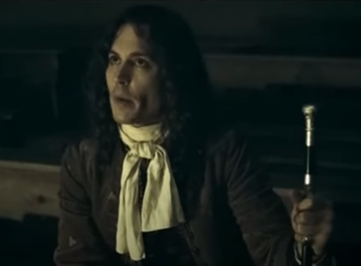 Screenshot: Johnny Deep with long hair wearing black shirt and white scarf is looking at side - from The Libertine (2004)
