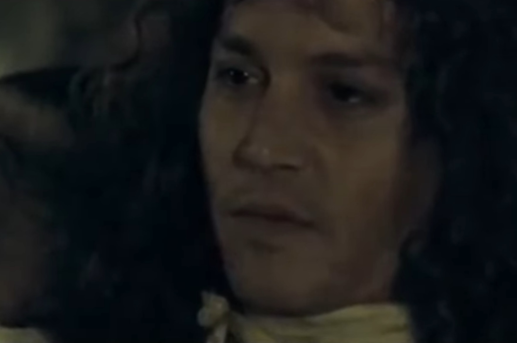 Screenshot: Johnny Deep with long hair wearing black shirt and white scarf is looking at side - from The Libertine (2004)