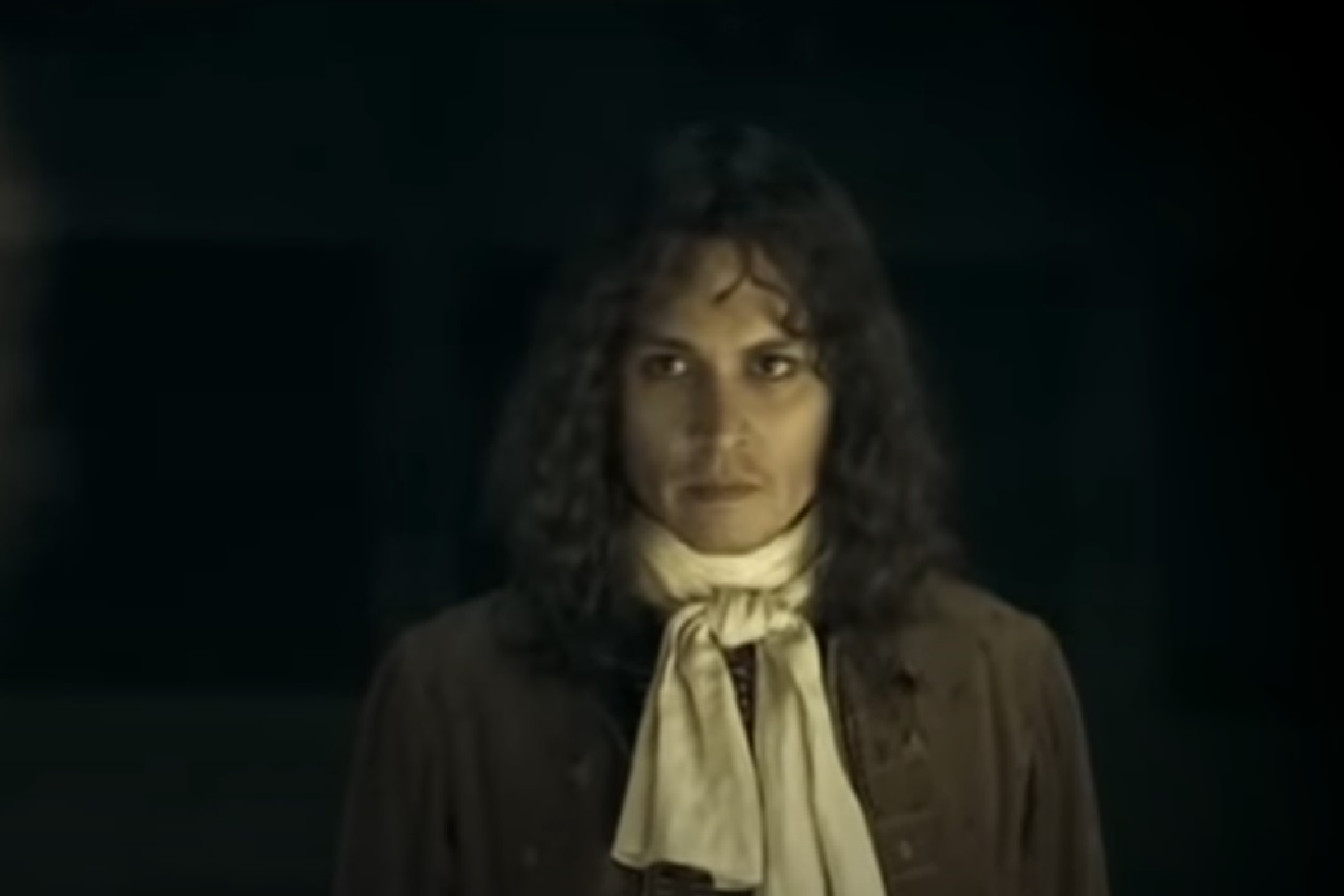 Screenshot: Johnny Deep with long hair wearing black shirt and white scarf is looking at front - from The Libertine (2004)
