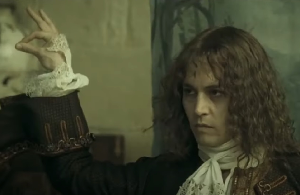Screenshot: Johnny Deep with long hair wearing black shirt and white scarf is looking at side - from The Libertine (2004)