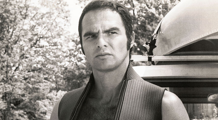 Grayscale photo of Burt Reynolds, in a scene from the 1972 film Deliverance with a truck and a canoe