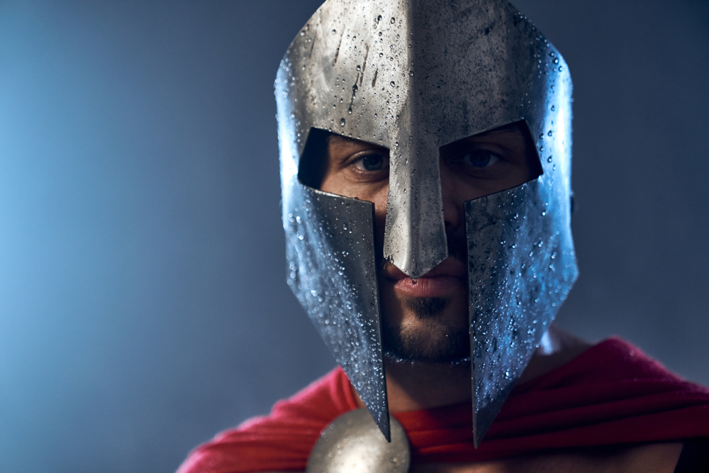Portrait of spartan warrior standing and looking at camera in red cloak and helmet with water drops