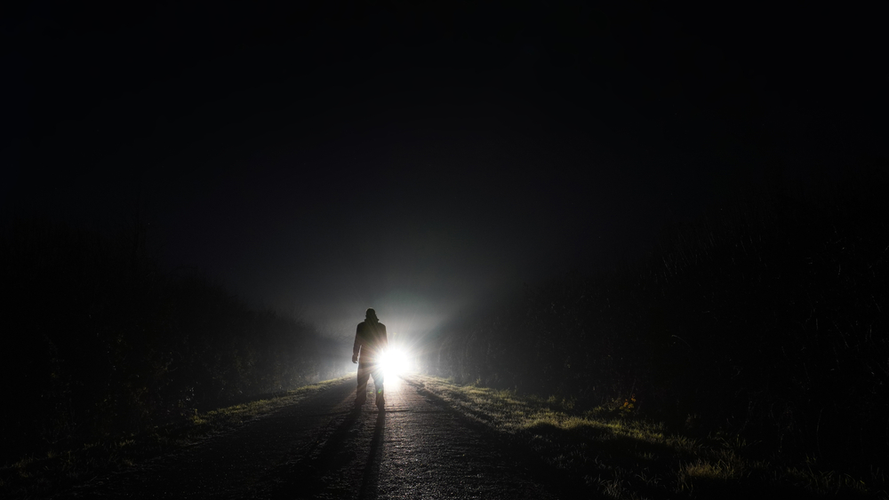 man on a road and car with lights in front of him
