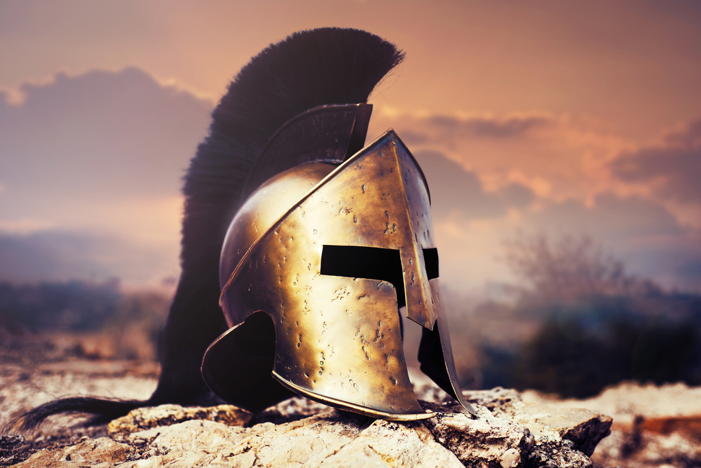Old Spartan helmet on rocks with sunset sky