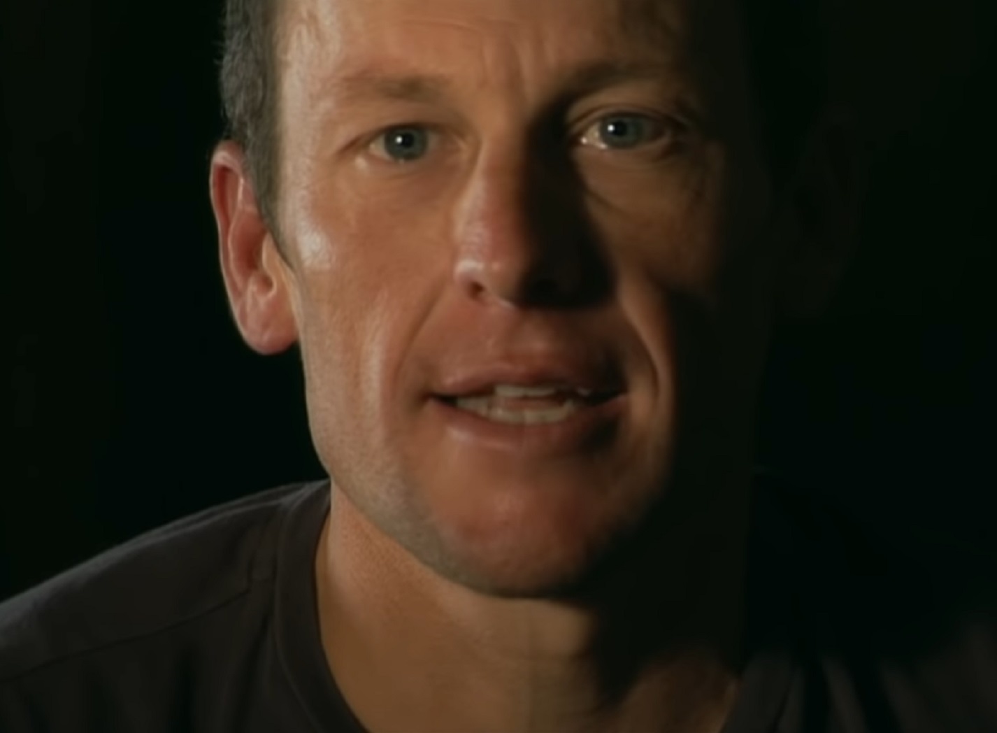 Screenshot: Lance Armstrong wearing black shirt is talking at camera - from The Armstrong Lie (2013)