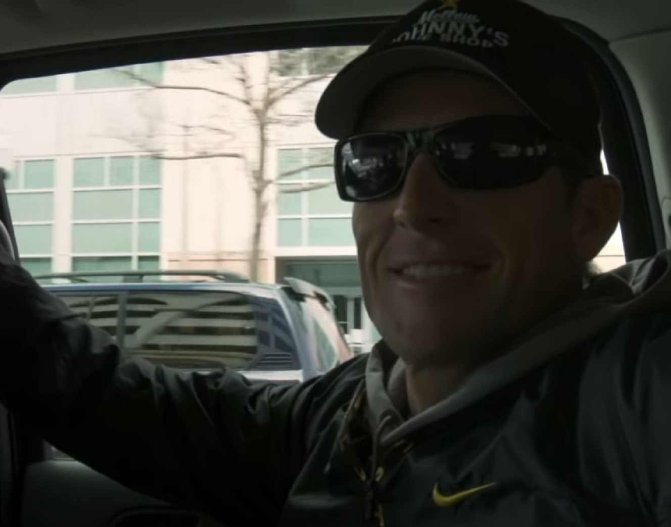 Screenshot: Lance Armstrong wearing sunglasses and hat is seating inside a car  - from Stop At Nothing- The Lance Armstrong Story (2014)