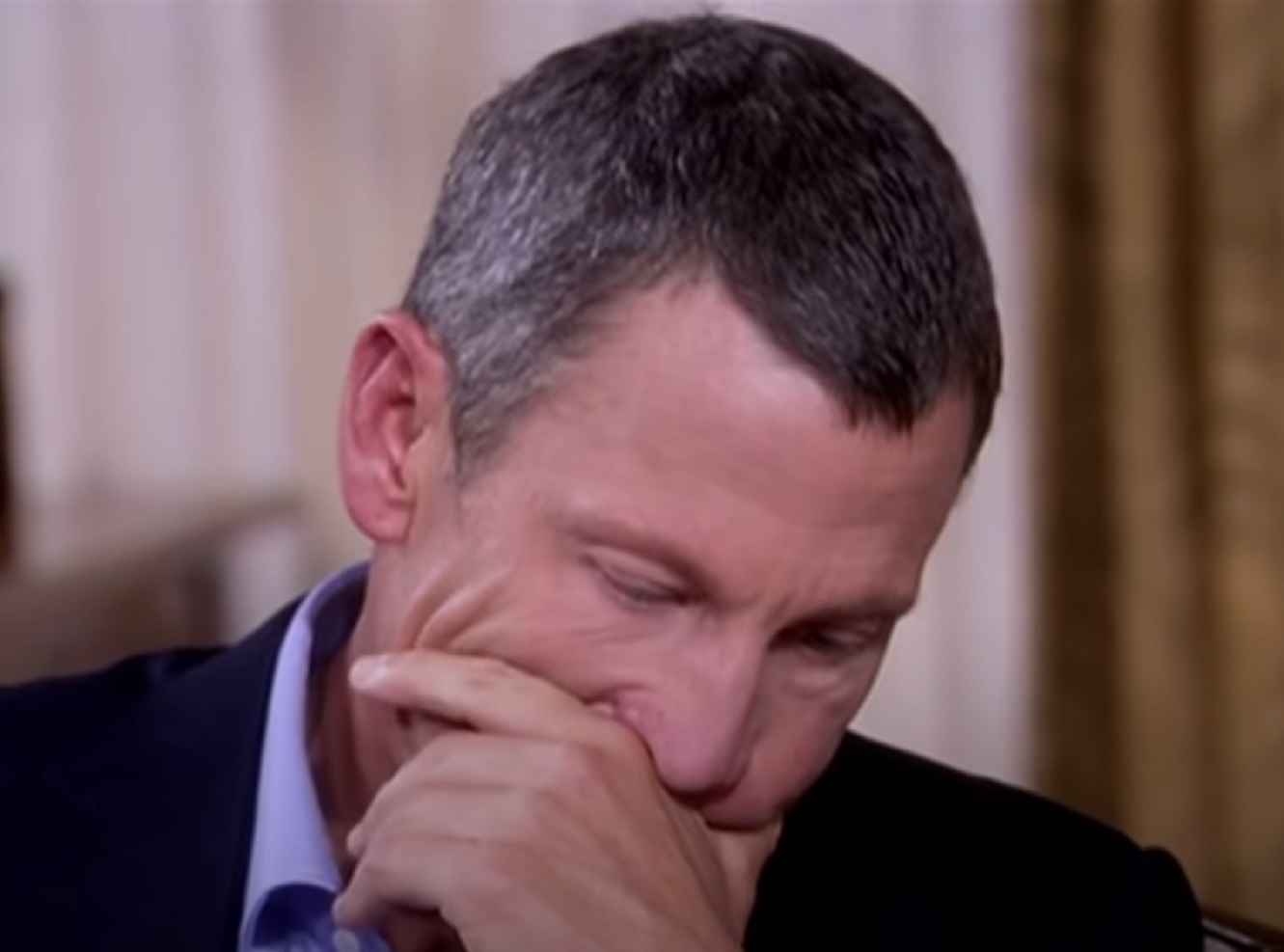 Screenshot: Lance Armstrong wearing blue shirt and black jacket is looking down upset - from Stop At Nothing- The Lance Armstrong Story (2014)