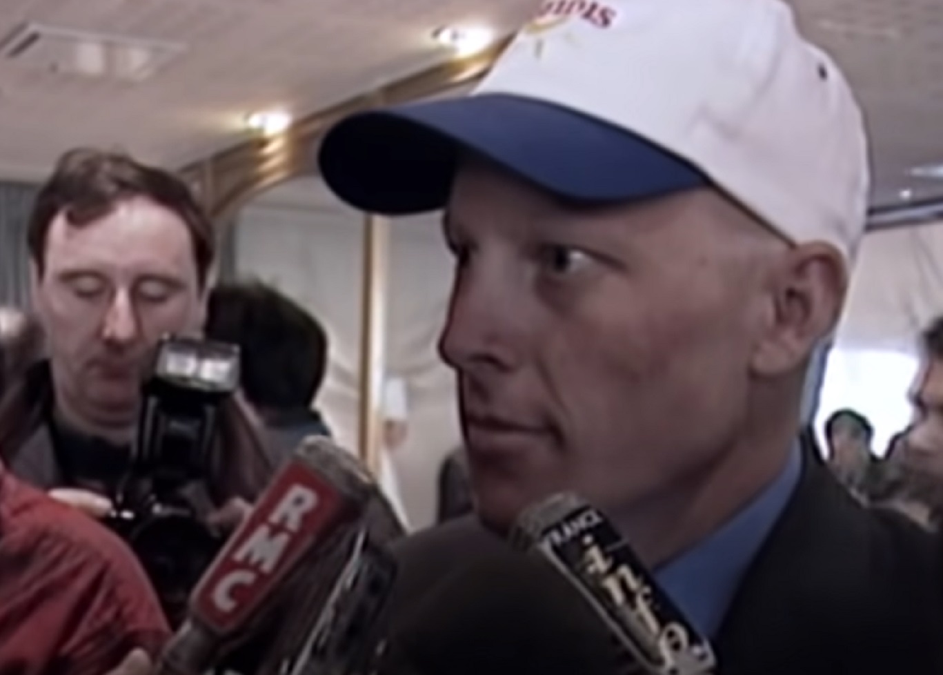 Screenshot: Lance Armstrong wearing white hat is talking on the microphone - from Stop At Nothing- The Lance Armstrong Story (2014).