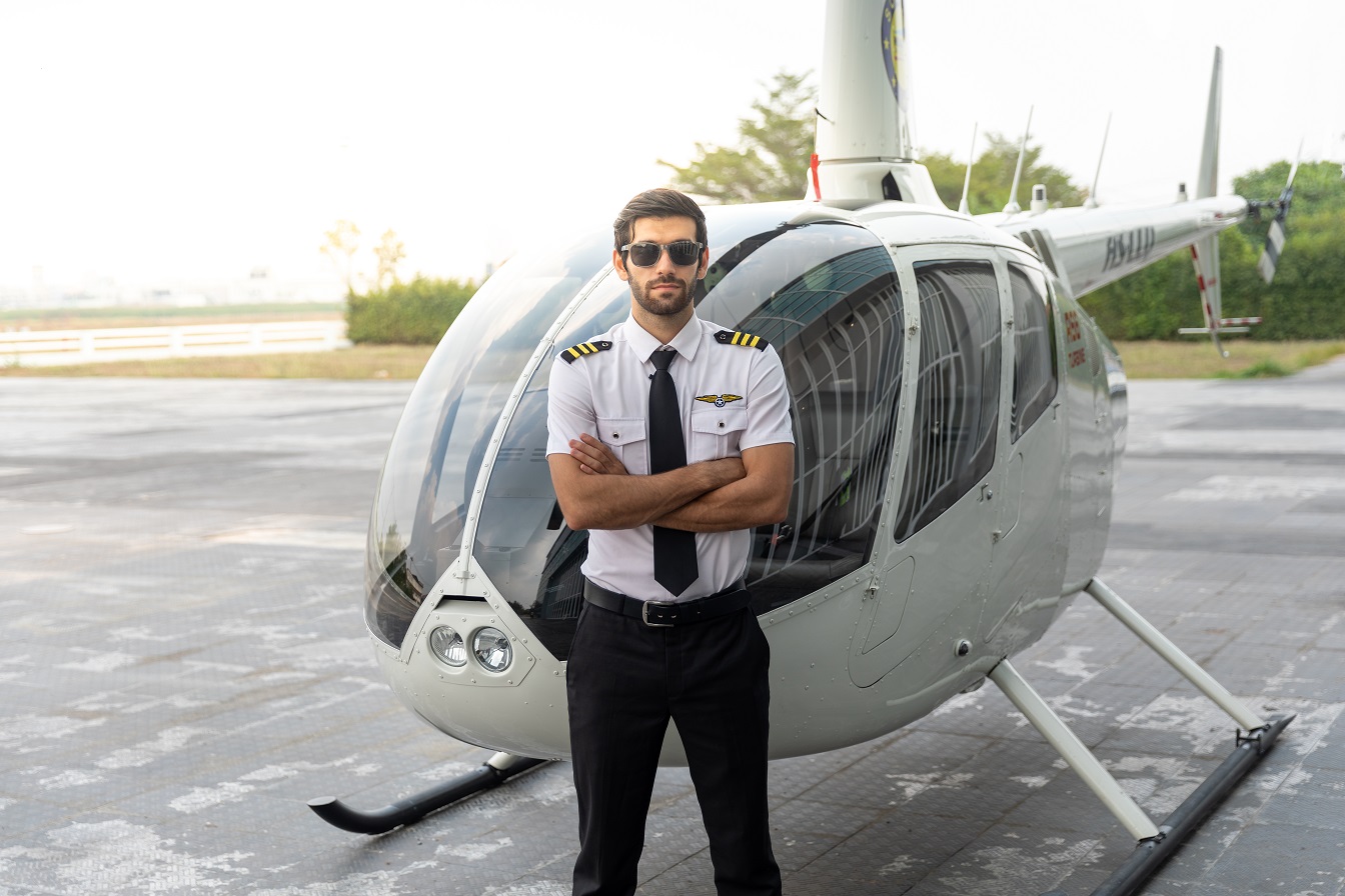 Helicopter pilot stands in front of a white helicopter.