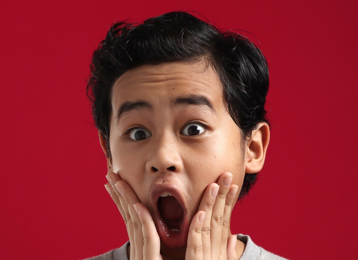 Young boy looking at camera with open mouth and big eyes.