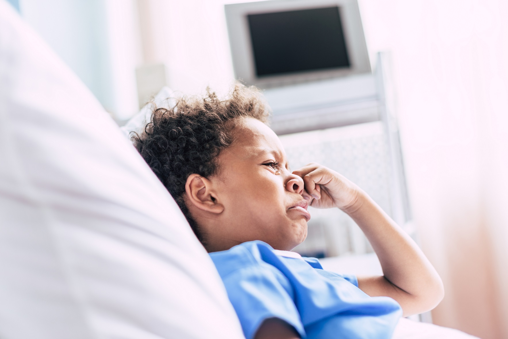Crying african boy lying in hospital bed.