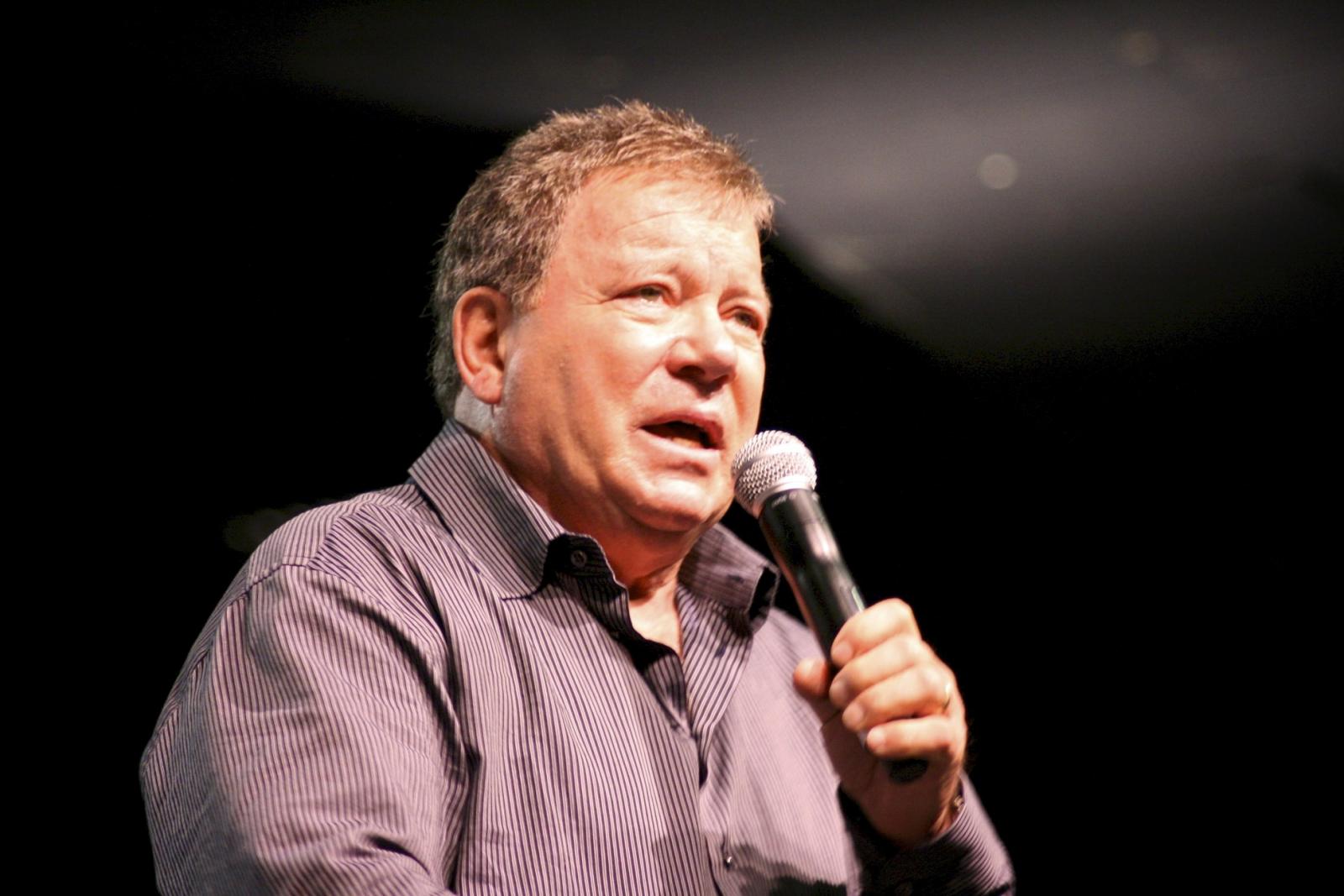 William Shatner wearing red shirt is talking.
