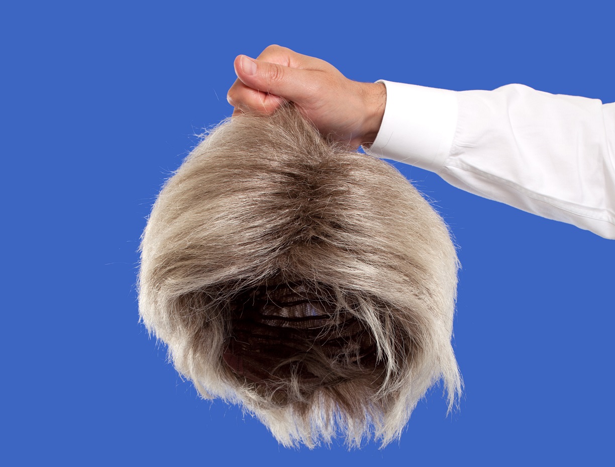 Hand holding a wig on a blue background.