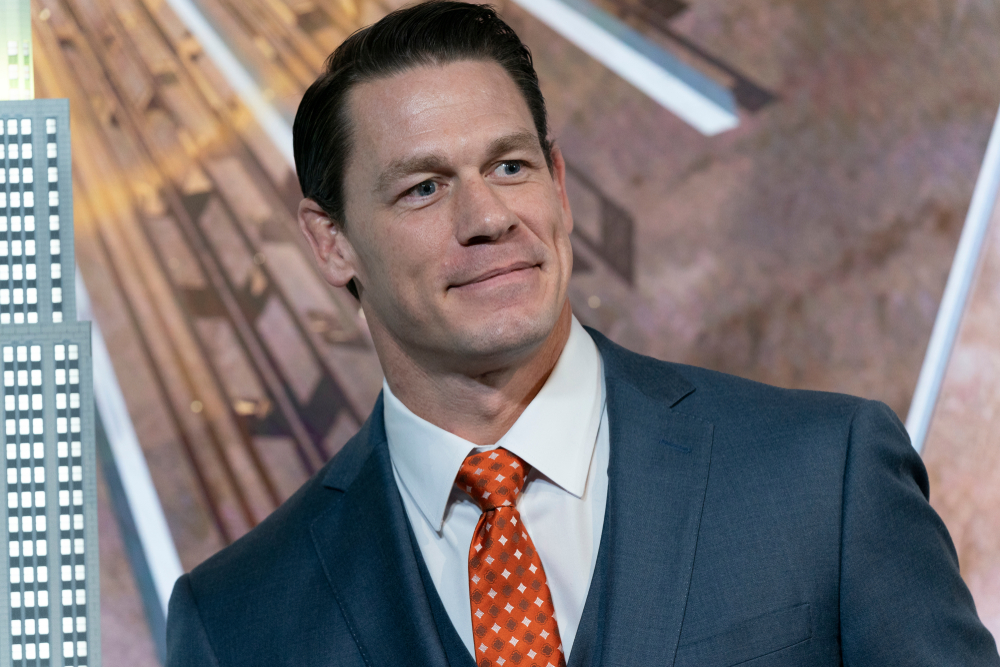 Actor John Cena wearing blue suit and a red tie smiling