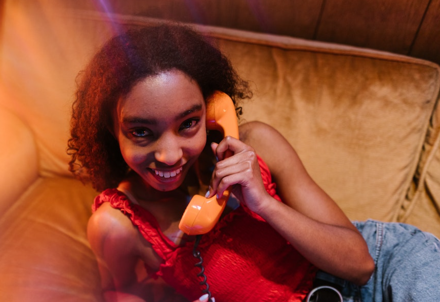 Young woman is smiling and speaking on orange telephone.