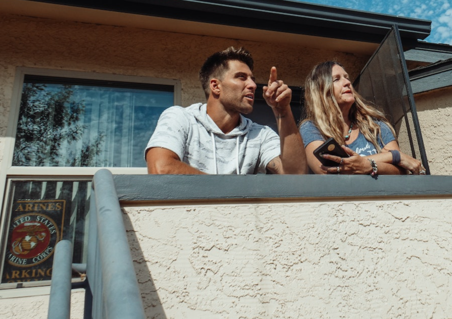 Man is standing on the balcony ,looking at side and talking with a woman.