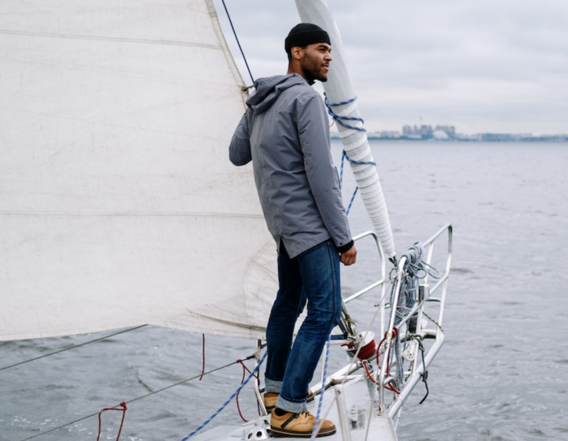 Man wearing grey jacket and hat is standing on a boat.