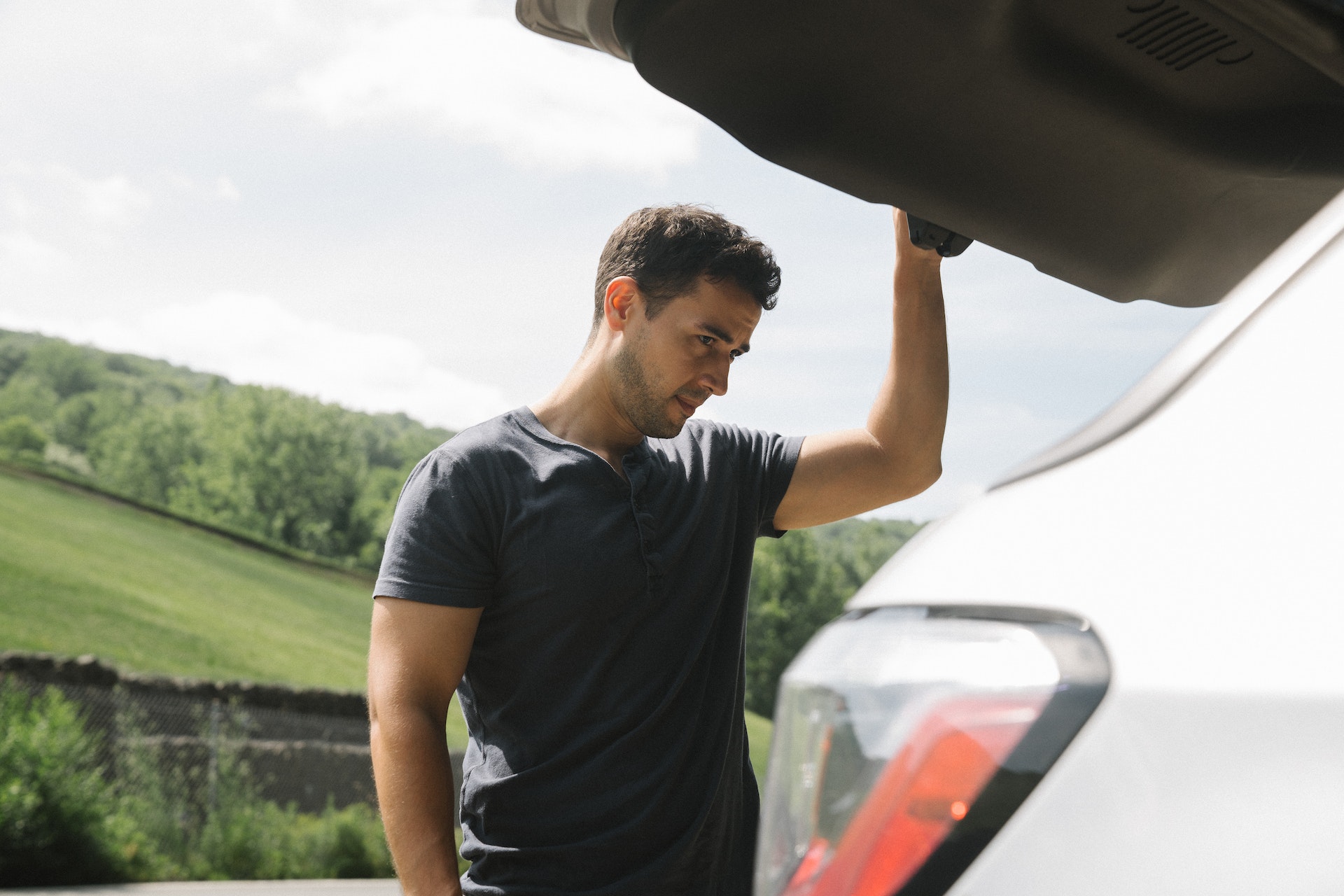 man looking in the car trunk wearing blue polo shirt with a green field in the background