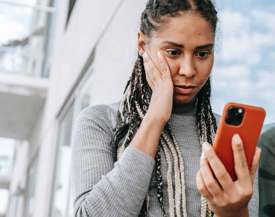 Black woman is reading message on the phone and looking shocked.