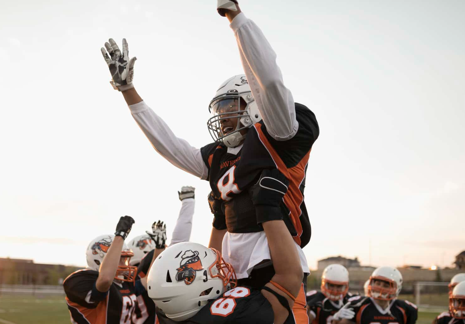 Teenage boy high school football players lifting celebrating, cheering teammate on football field