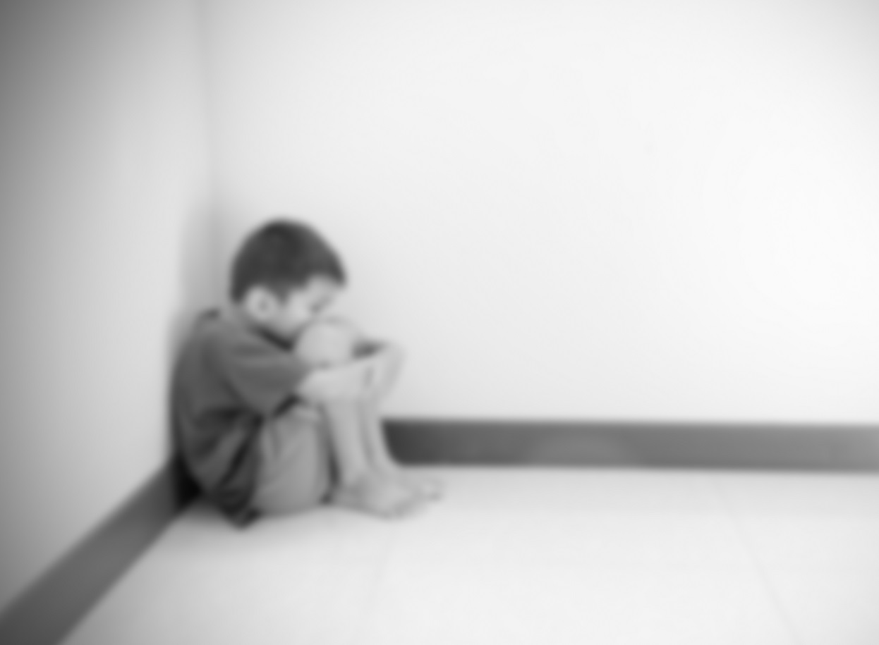 Blurred boy hugged his knees in a corner of the room.