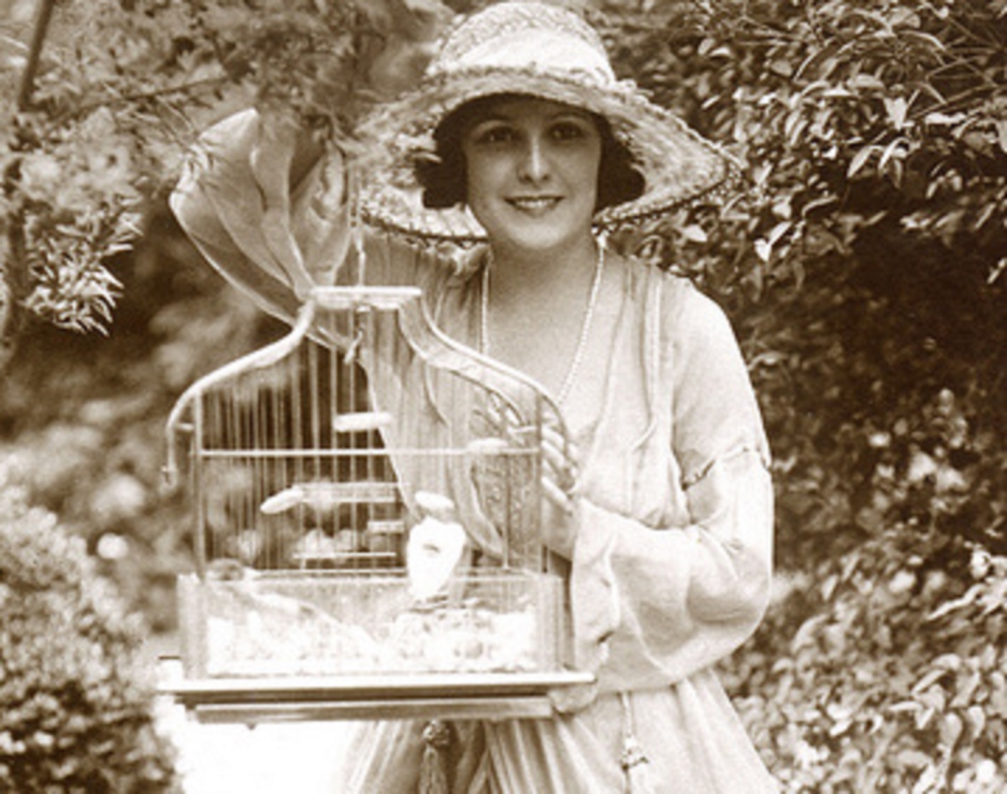 Lucy, Lady Duff-Gordon is holding a cage In The Garden.
