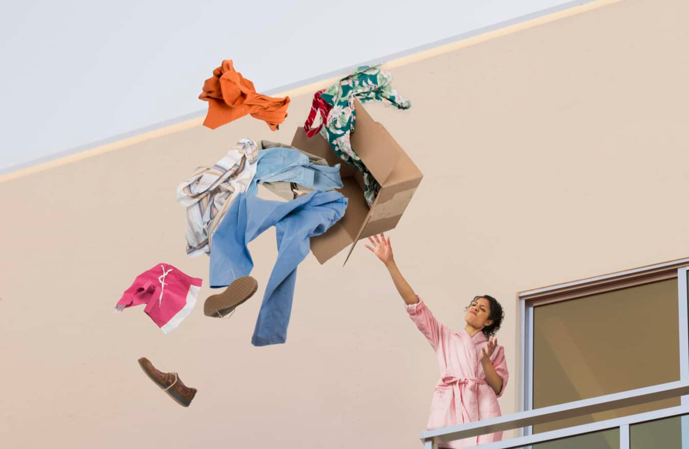 Mixed race woman throwing clothes off balcony.