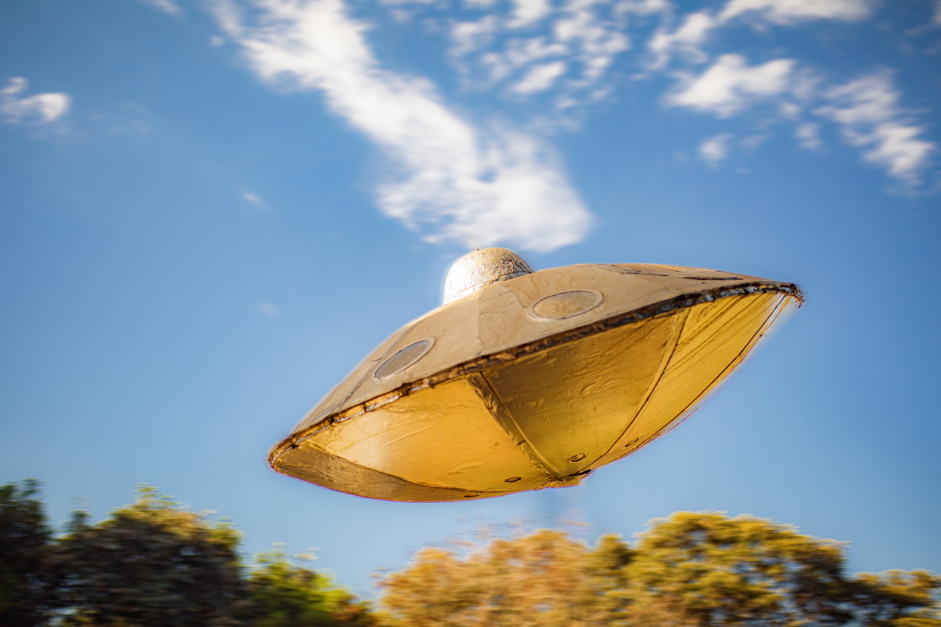 golden yellow UFO toy in floating in the air on a blue sky