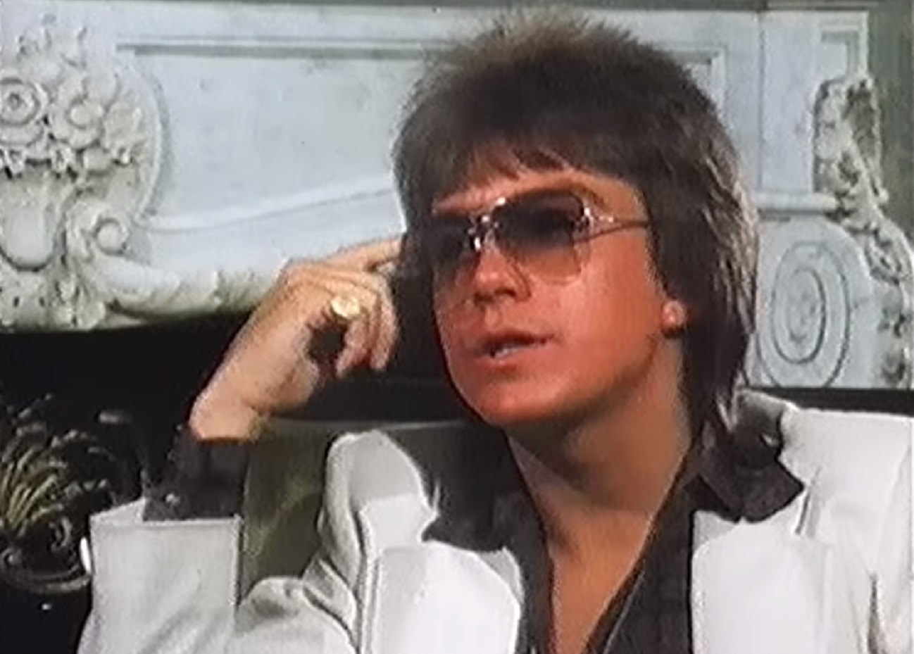 Screenshot: David Cassidy wearing white suit and glasses is talking - from David Cassidy - The Last Session (2018).