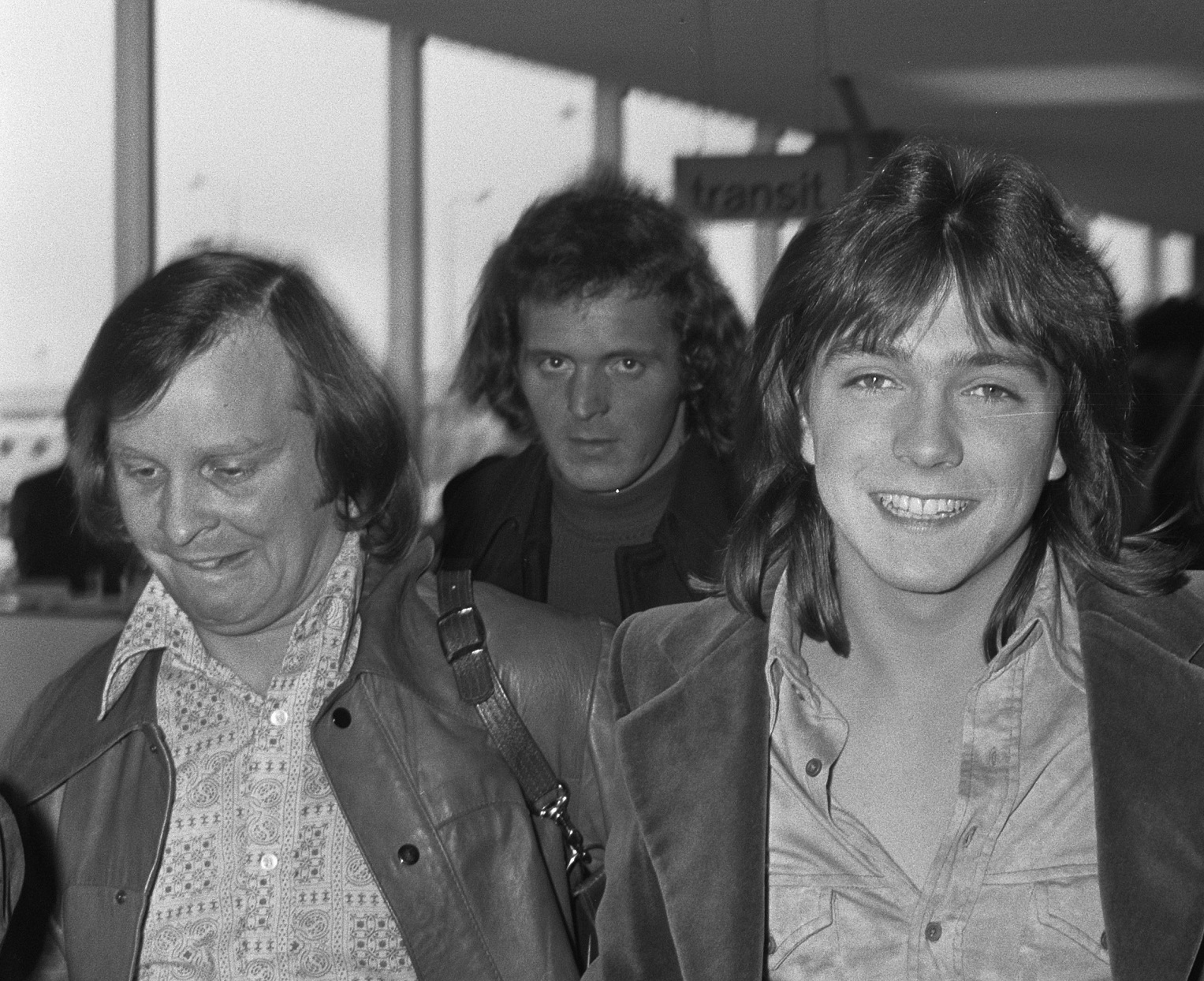 David Cassidy wearing grey shirt and jacket is smiling while walking at airport - 1973