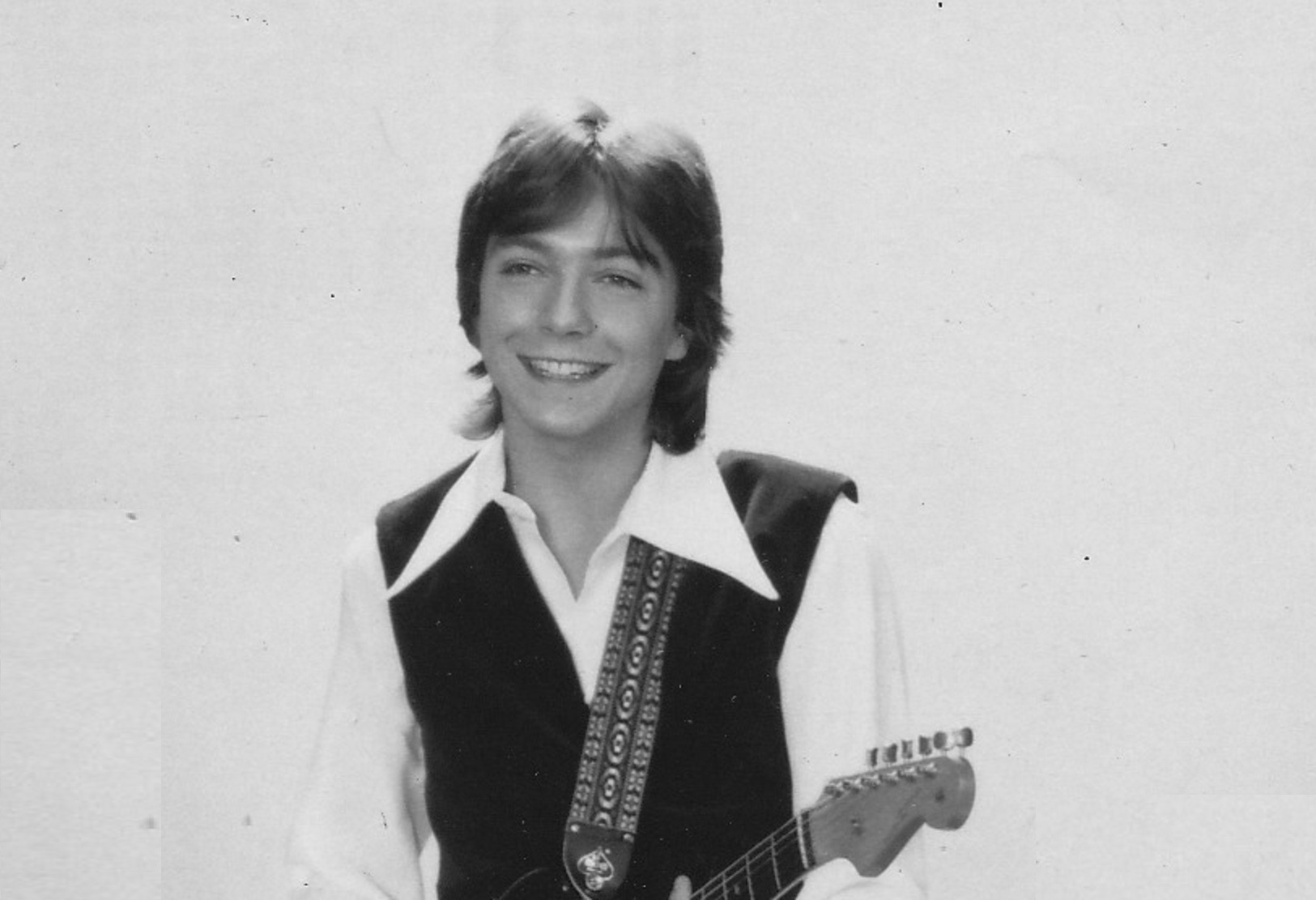 David Cassidy wearing white shirt and guitar is looking at front and smiling - 1970