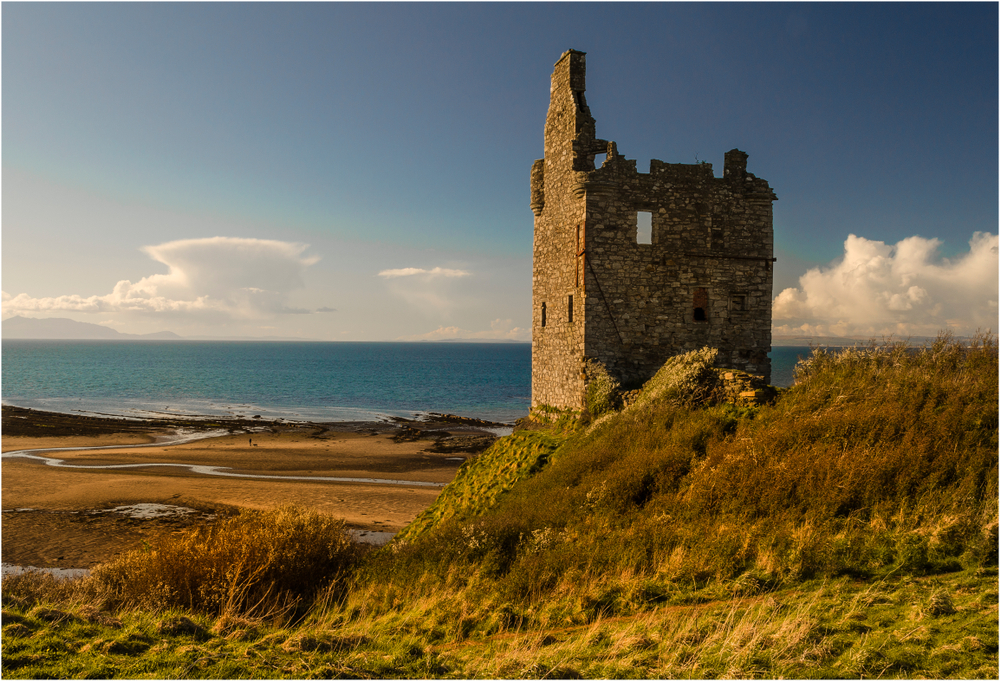 photo of greenan castle in ayr scotland with green field in front and blue see and cloudy sky