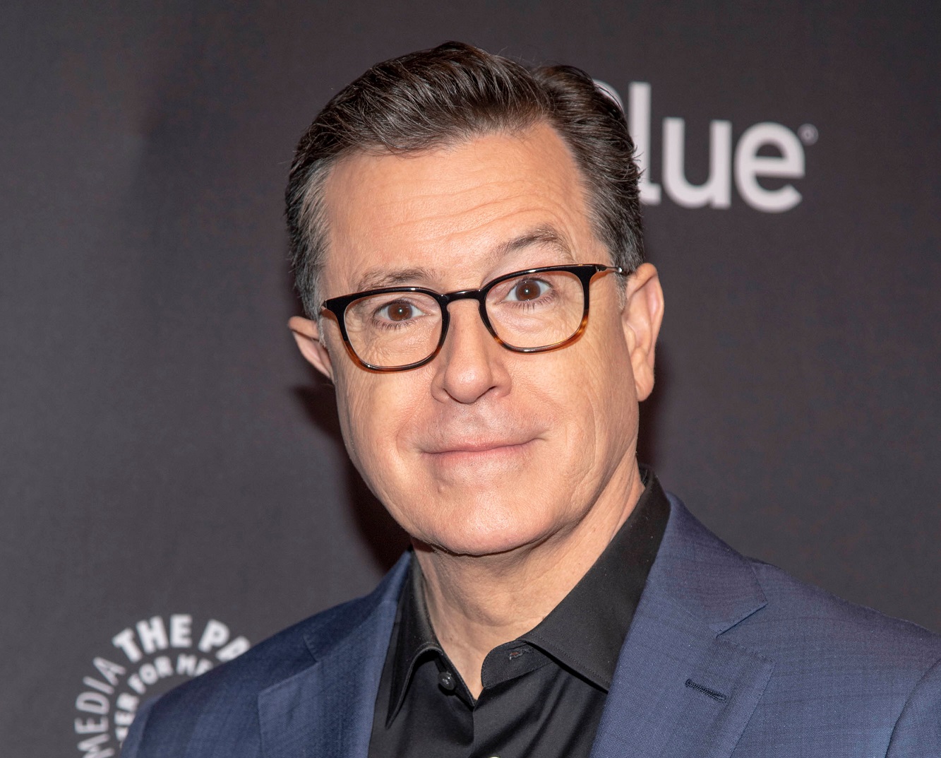 Stephen Colbert wearing blue suit is looking and smiling at camera - 2019