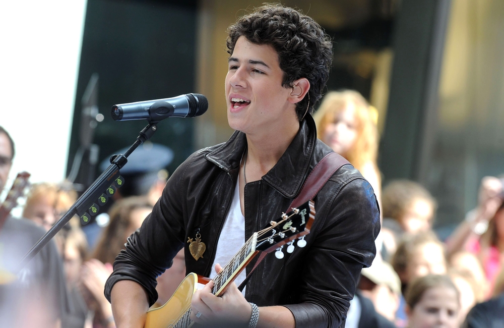 Nick Jonas at talk show appearance playing a guitar and singing
