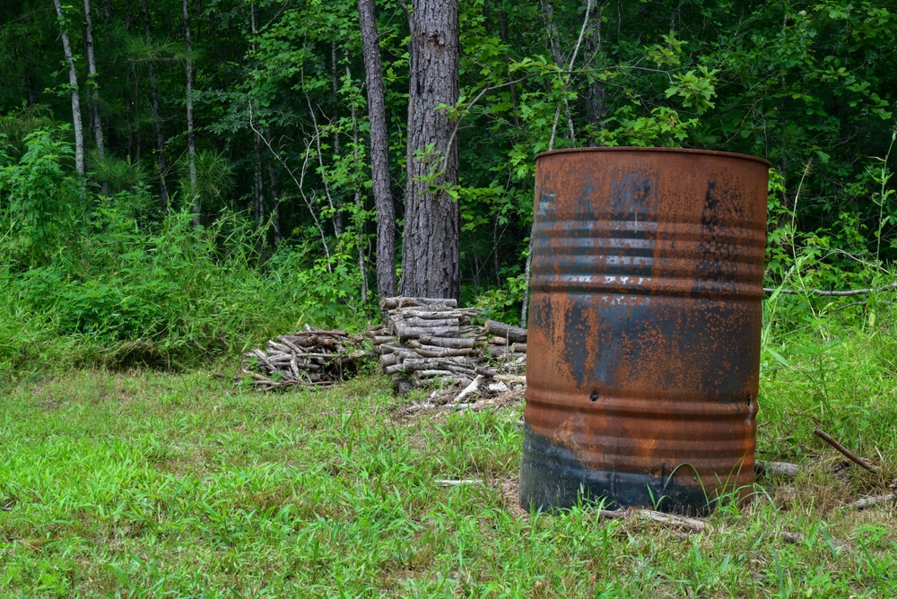 old rusted burn barrel placed on a green grass surrounded by trees