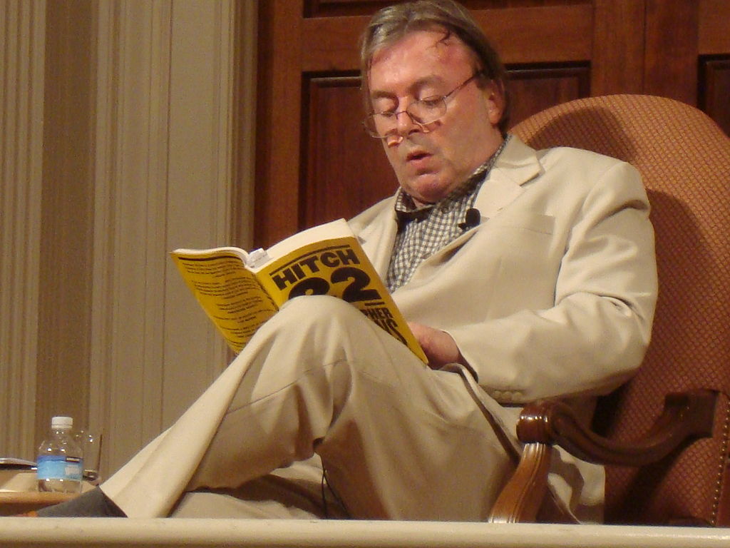 British author and journalist Christopher Hitchens reading his book Hitch 22 sitting on a chair wearing a beige suit