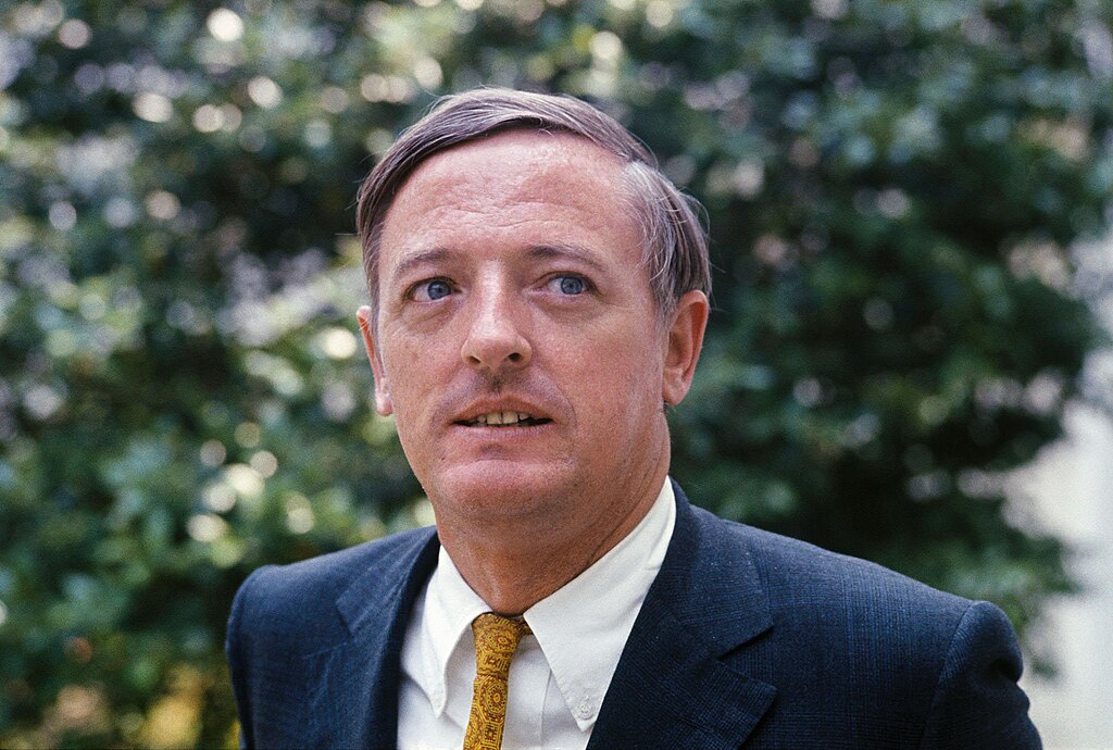 Portrait Photo Of  William F. Buckley Jr wearing a blue suit white shirt and yellow tie facing the camera
