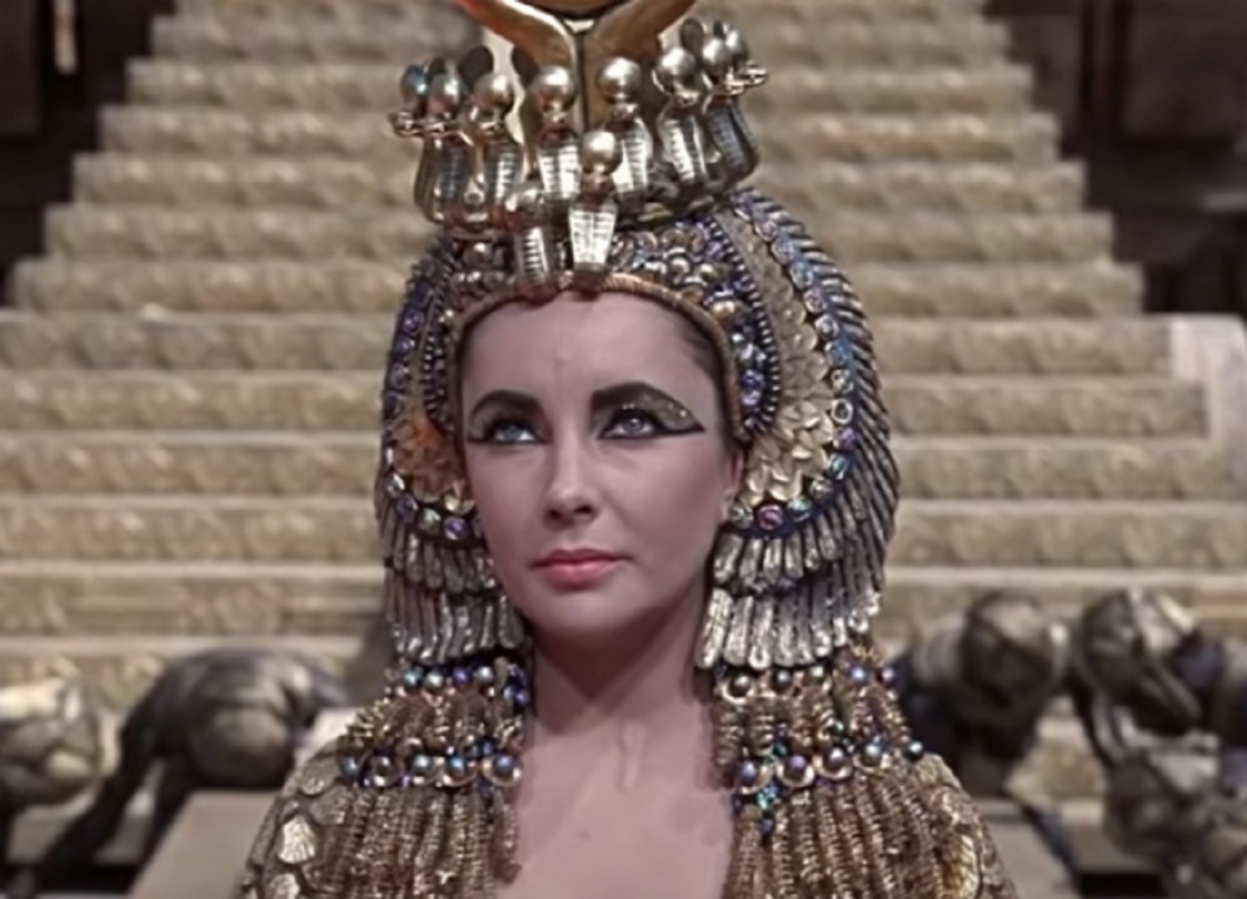 Screenshot: (Elizabeth Taylor) Cleopatra wearing golden crown is looking at side - from Cleopatra (1963)