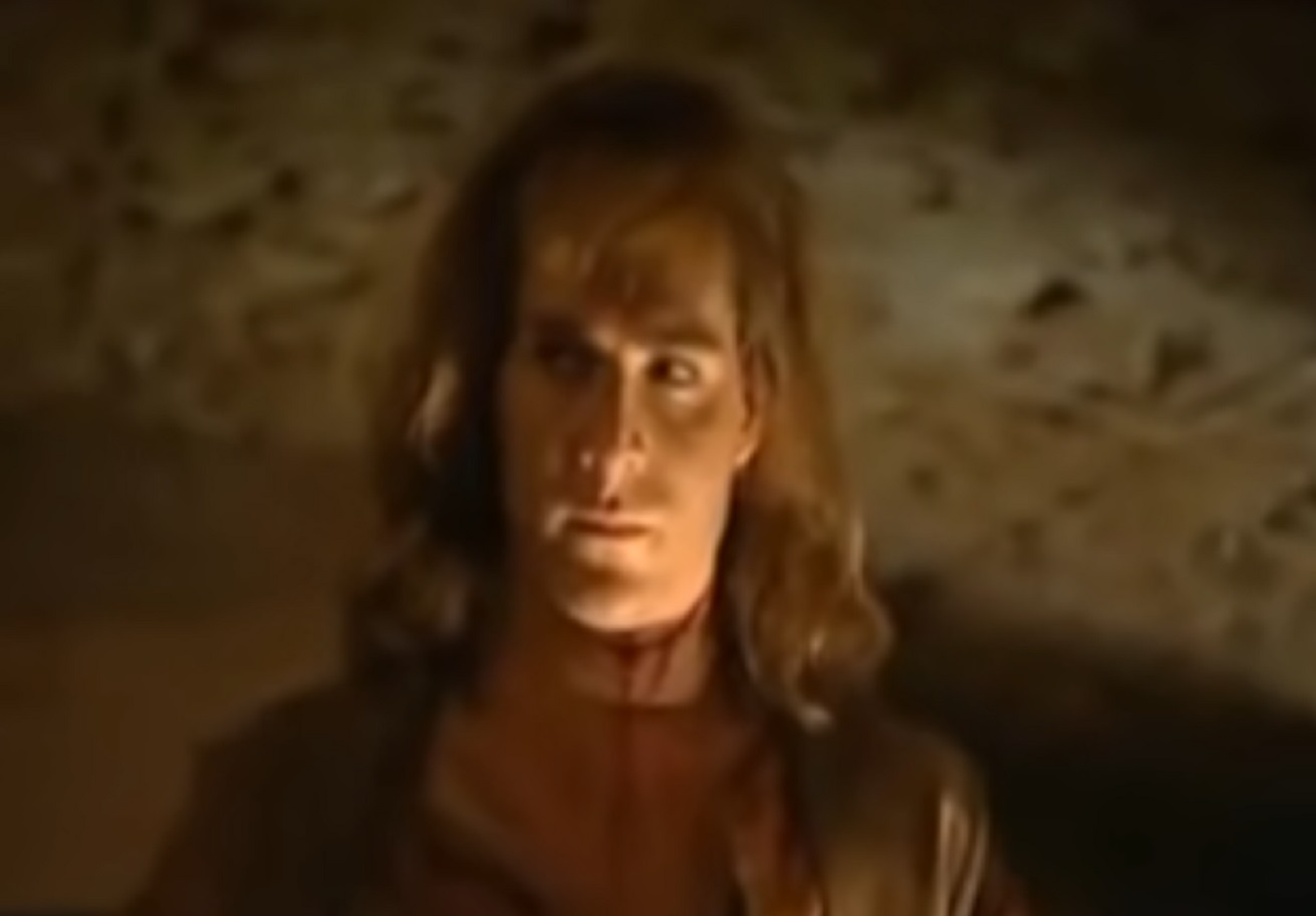 Screenshot: (Mark Umbers) Perkin Warbeck with long hair is looking at side - from Princes in the Tower (2005).