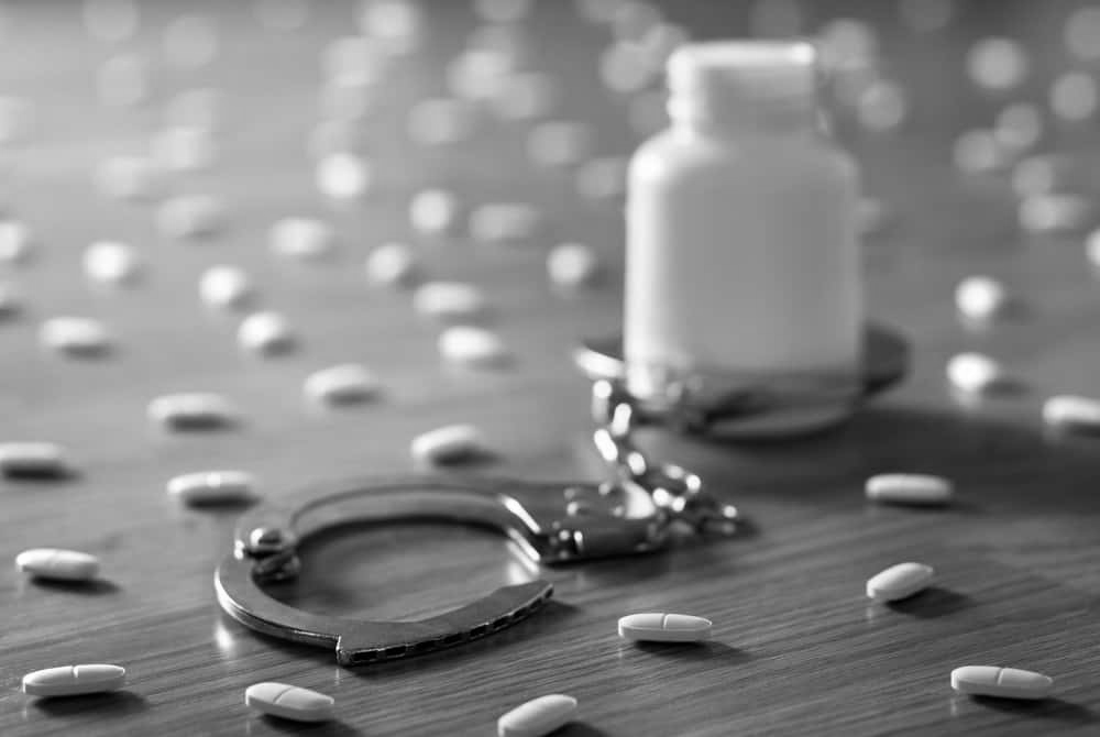Medicine bottle handcuffed and surrounded by many pills depicting medical abuse