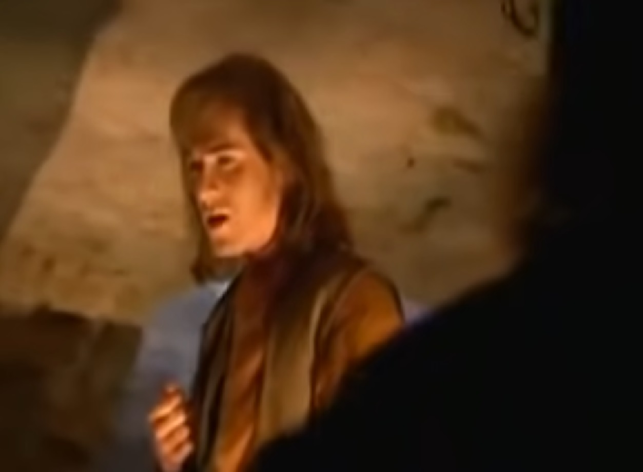 Screenshot: (Mark Umbers) Perkin Warbeck with long hair is talking with other person in jail - from Princes in the Tower (2005).